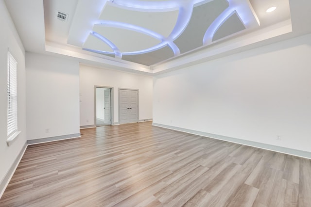 empty room with baseboards, a raised ceiling, and light wood-style floors