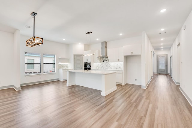 kitchen featuring tasteful backsplash, wall chimney range hood, light wood-type flooring, light countertops, and white cabinetry