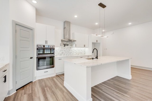 kitchen with backsplash, double oven, light wood-style flooring, wall chimney exhaust hood, and a sink