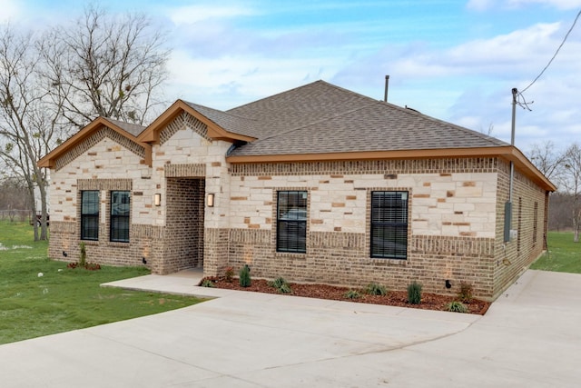 view of front of house with brick siding, roof with shingles, and a front yard