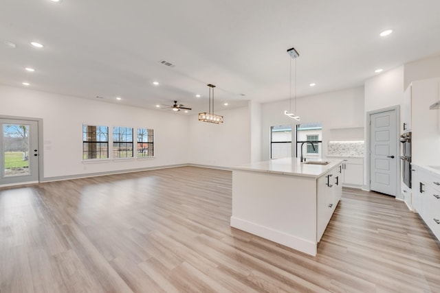 kitchen featuring visible vents, an island with sink, recessed lighting, white cabinets, and a sink