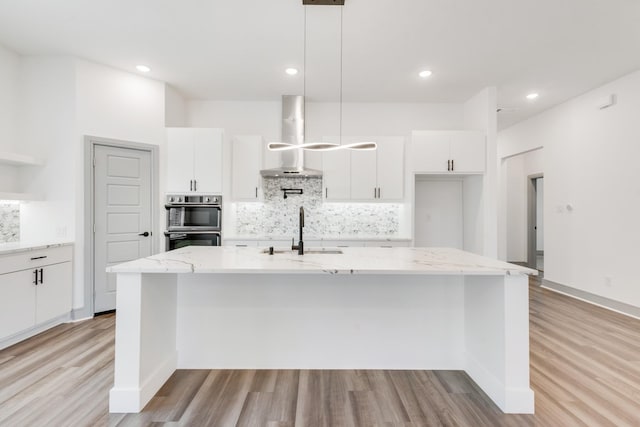 kitchen with white cabinets, wall chimney exhaust hood, light wood-style flooring, and a sink