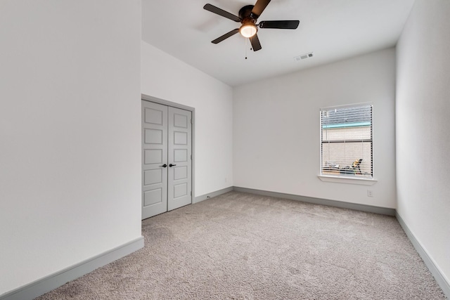 empty room featuring light carpet, visible vents, a ceiling fan, and baseboards