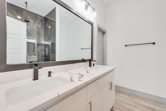 bathroom featuring double vanity, wood finished floors, a walk in shower, and a sink