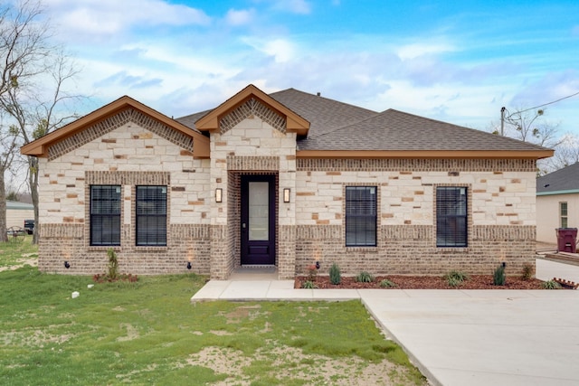 view of front of house with brick siding, roof with shingles, and a front lawn