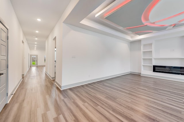 unfurnished living room featuring light wood-type flooring, built in shelves, baseboards, and a glass covered fireplace