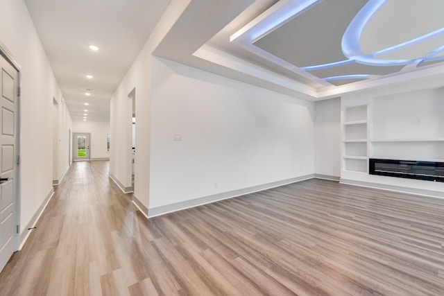 unfurnished living room with built in shelves, light wood-style flooring, a glass covered fireplace, recessed lighting, and baseboards