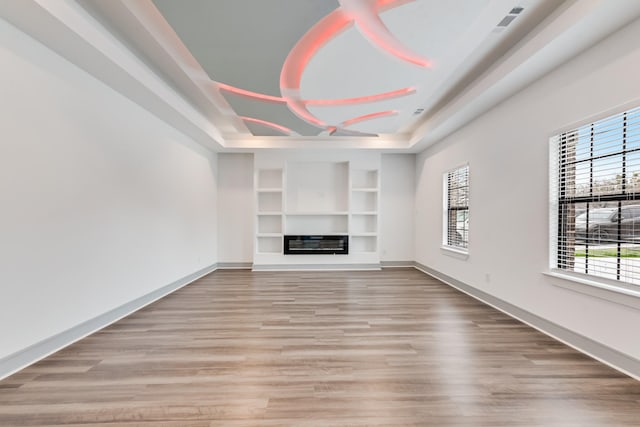 unfurnished living room featuring built in features, a healthy amount of sunlight, light wood-type flooring, and baseboards