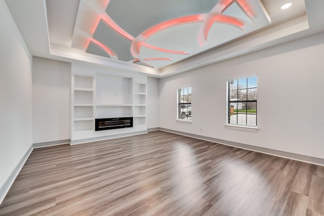 unfurnished living room with a raised ceiling, baseboards, and wood finished floors