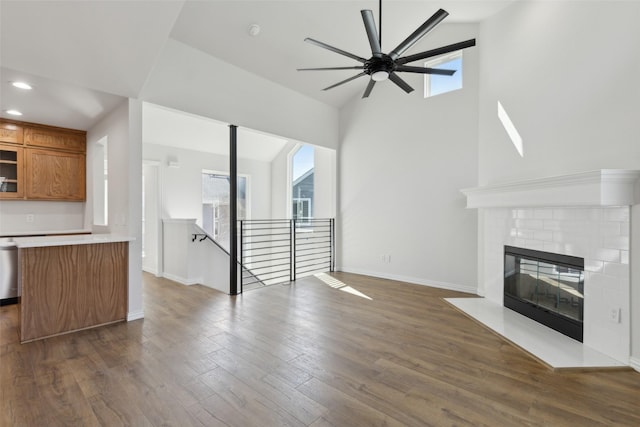 unfurnished living room featuring a ceiling fan, baseboards, dark wood finished floors, recessed lighting, and a tile fireplace