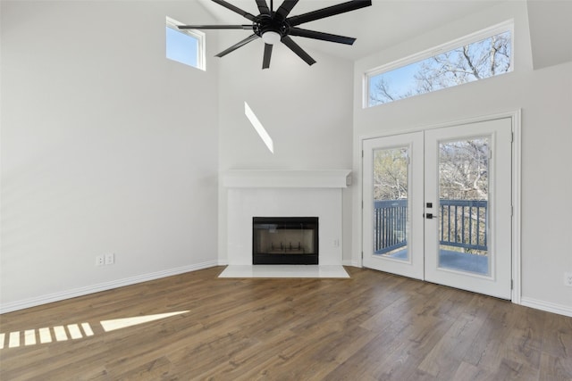 unfurnished living room featuring a fireplace with flush hearth, wood finished floors, french doors, baseboards, and a towering ceiling