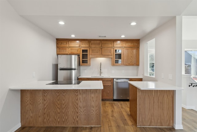 kitchen with visible vents, a sink, stainless steel appliances, a peninsula, and brown cabinetry