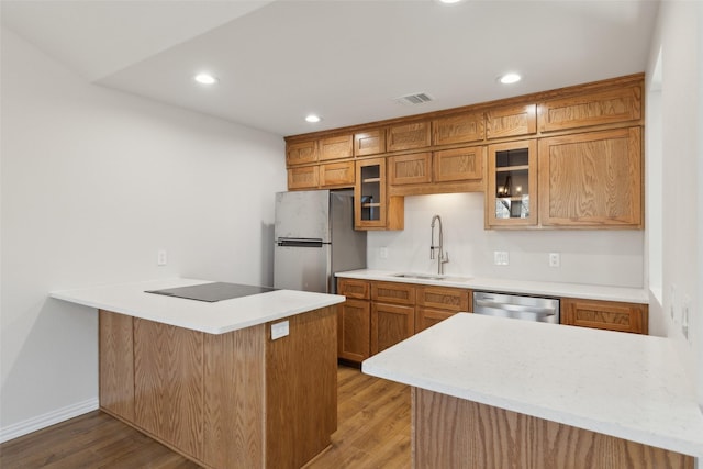 kitchen with a peninsula, light wood-style flooring, appliances with stainless steel finishes, and a sink