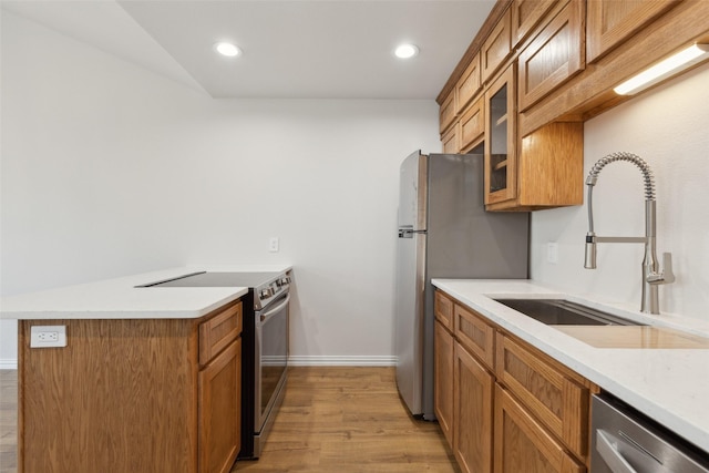 kitchen featuring brown cabinetry, appliances with stainless steel finishes, a peninsula, and a sink