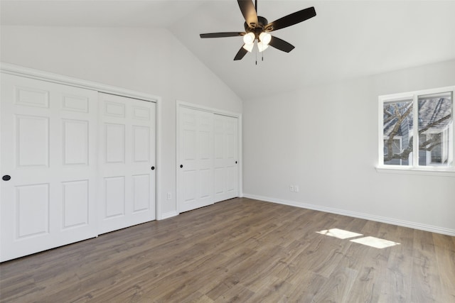 unfurnished bedroom featuring a ceiling fan, wood finished floors, baseboards, vaulted ceiling, and two closets