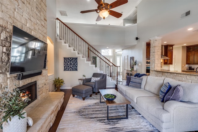 living room with visible vents, a stone fireplace, stairs, and wood finished floors