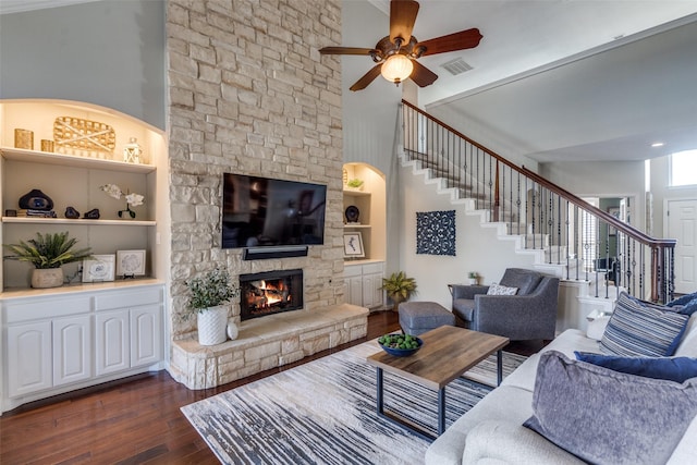 living area with visible vents, dark wood-type flooring, ceiling fan, stairway, and a stone fireplace