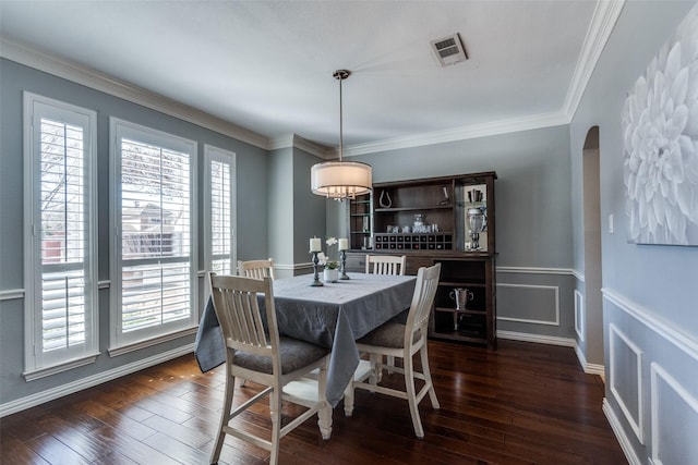 dining space featuring dark wood-type flooring, crown molding, arched walkways, and visible vents