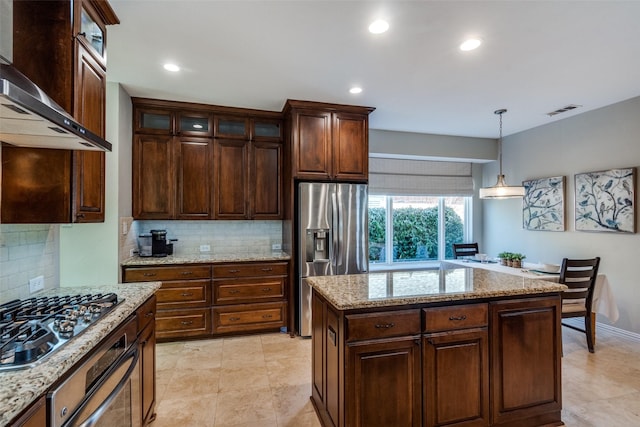 kitchen featuring visible vents, appliances with stainless steel finishes, wall chimney exhaust hood, glass insert cabinets, and hanging light fixtures