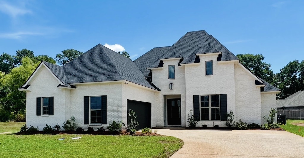 french country home with a front yard, an attached garage, brick siding, and driveway