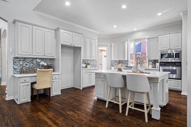 kitchen with dark wood-type flooring, a breakfast bar area, light countertops, appliances with stainless steel finishes, and arched walkways