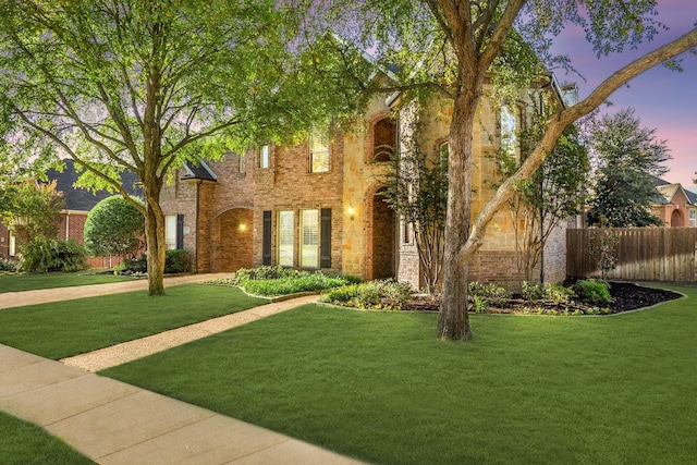 view of front facade featuring a yard, fence, and brick siding