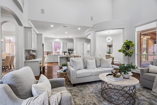 living area with dark wood finished floors, visible vents, arched walkways, and a towering ceiling