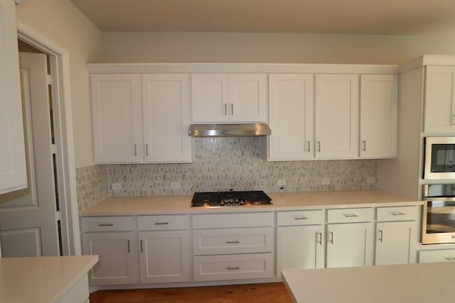 kitchen with under cabinet range hood, stainless steel appliances, light countertops, and tasteful backsplash