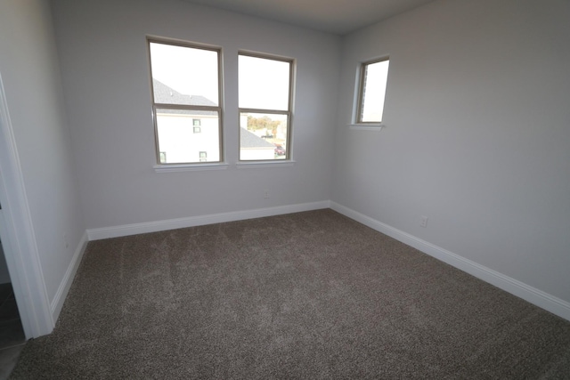 spare room featuring baseboards and dark carpet