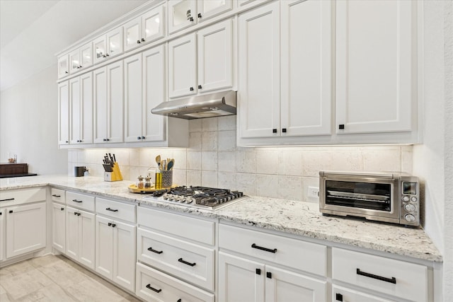 kitchen featuring stainless steel gas cooktop, a toaster, decorative backsplash, white cabinets, and under cabinet range hood