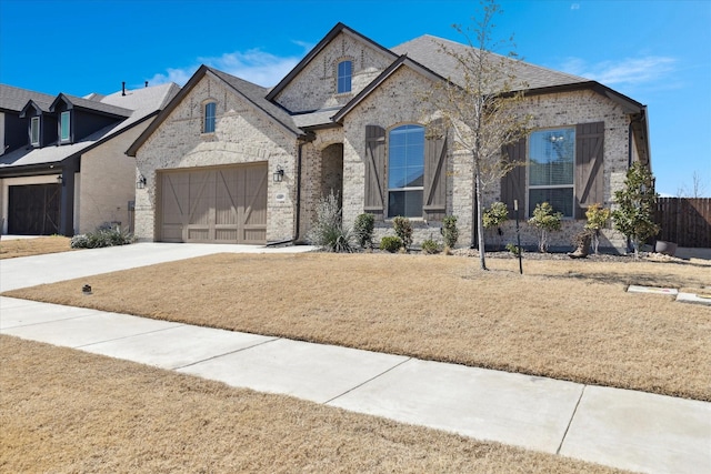 french country home with a garage, brick siding, concrete driveway, and a front lawn