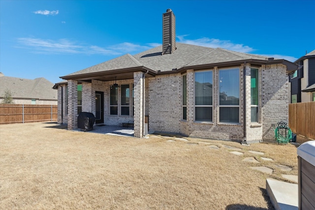 back of property featuring brick siding, a chimney, a fenced backyard, and roof with shingles