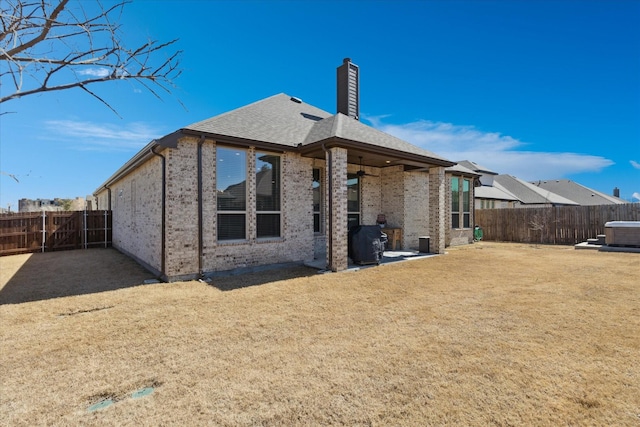 rear view of property with a patio, brick siding, a fenced backyard, and a chimney