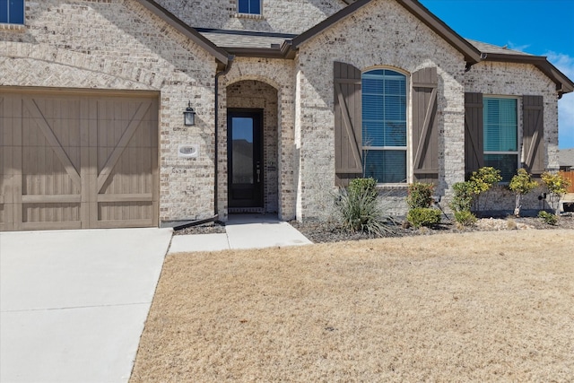 doorway to property with a garage, brick siding, and roof with shingles