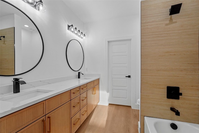 bathroom featuring a sink, a tub to relax in, wood finished floors, and double vanity