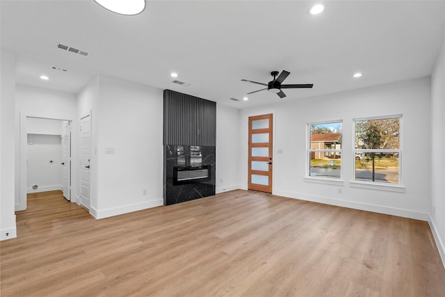 unfurnished living room with a high end fireplace, visible vents, and light wood finished floors