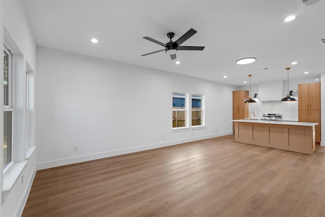 unfurnished living room featuring a ceiling fan, baseboards, recessed lighting, a sink, and light wood-style floors