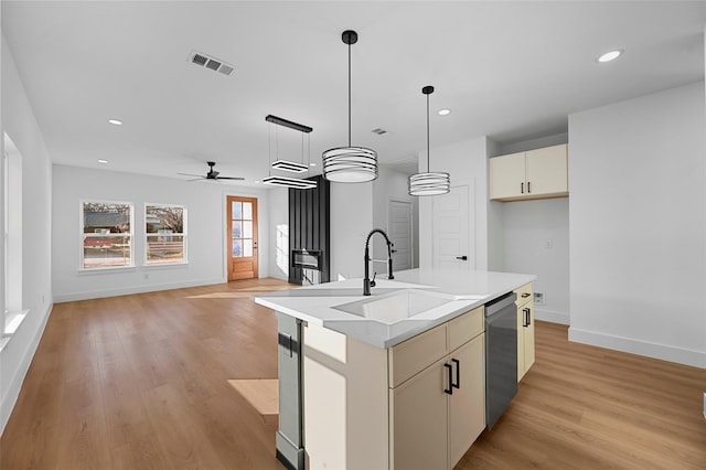 kitchen featuring visible vents, a sink, stainless steel dishwasher, decorative light fixtures, and light wood-type flooring