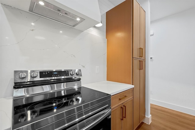 kitchen with brown cabinets, stainless steel range with electric stovetop, light wood-style flooring, baseboards, and extractor fan