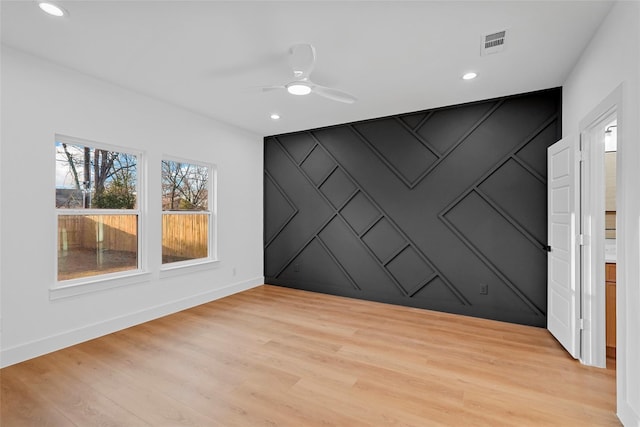 unfurnished room with an accent wall, light wood-style flooring, a decorative wall, and visible vents