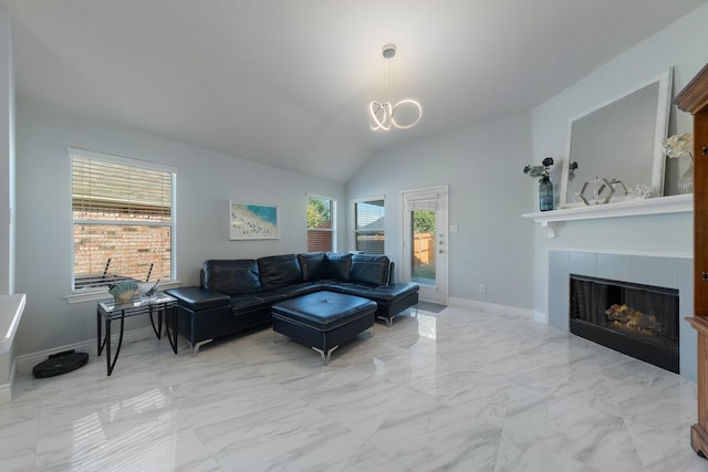 living area featuring a notable chandelier, marble finish floor, baseboards, a tile fireplace, and vaulted ceiling