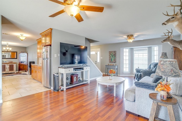 living area with baseboards, light wood-style flooring, and ceiling fan with notable chandelier