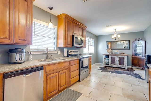 kitchen featuring brown cabinetry, visible vents, a sink, appliances with stainless steel finishes, and decorative light fixtures