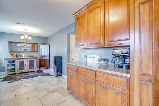 kitchen featuring a notable chandelier, light stone countertops, visible vents, and brown cabinets