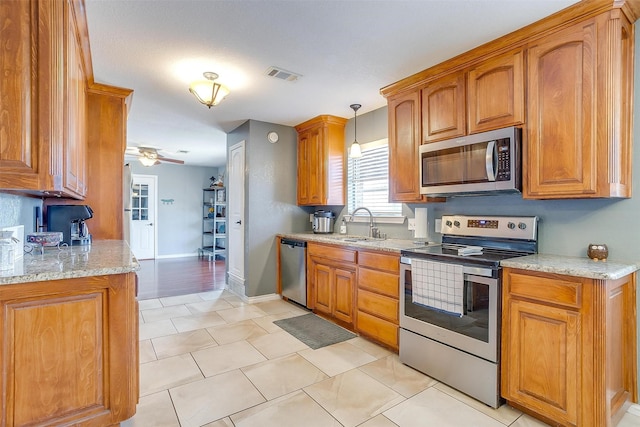 kitchen with visible vents, a sink, light stone counters, stainless steel appliances, and brown cabinetry