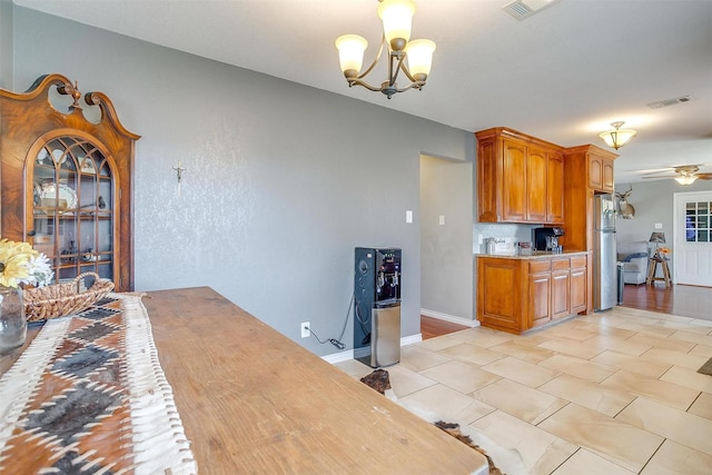 kitchen featuring visible vents, light countertops, ceiling fan with notable chandelier, freestanding refrigerator, and brown cabinetry