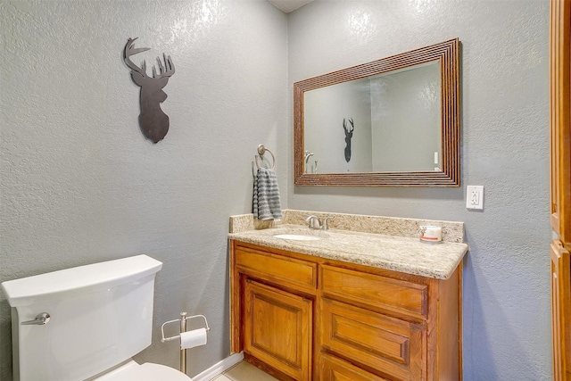 half bathroom with toilet, vanity, and a textured wall