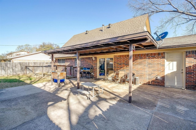 rear view of house with a patio area, brick siding, roof with shingles, and fence