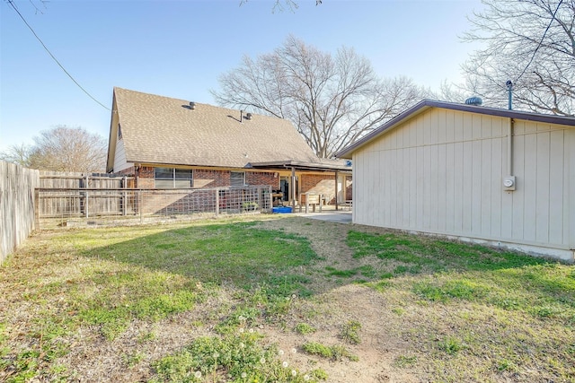 rear view of property with fence, a yard, a shingled roof, a patio area, and brick siding