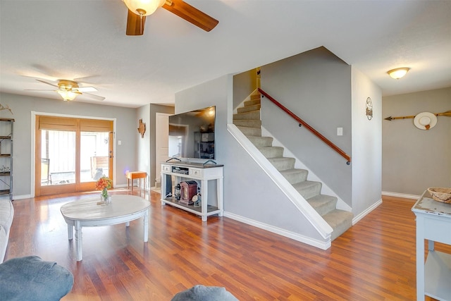 living area with stairway, wood finished floors, baseboards, and ceiling fan